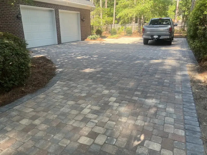 Paver driveway running up to a two-car garage beside a brick house