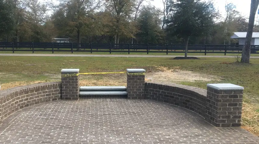 Dark brick paver patio enclosed by a curved brick seating wall with capped piers