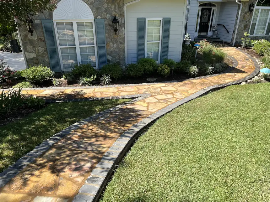 Curved flagstone walkway with a dark paver border running through a lawn to a stone-faced house