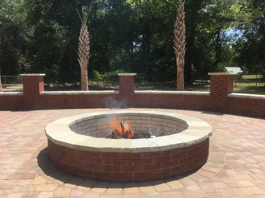 Round brick fire pit with a stone cap burning on a paver patio inside a brick seating wall