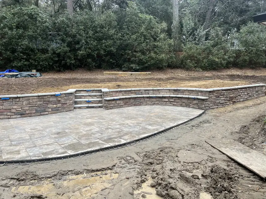 Stacked stone retaining wall with steps and a seat ledge curving around a new paver patio