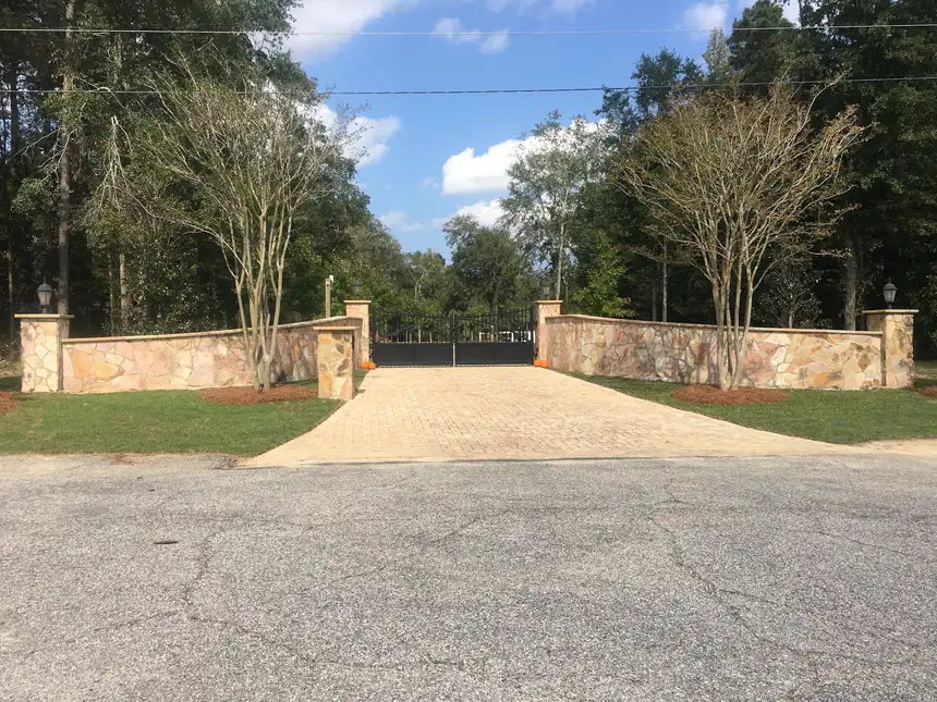Flagstone-faced entry walls with capped piers flanking a paver driveway and gate